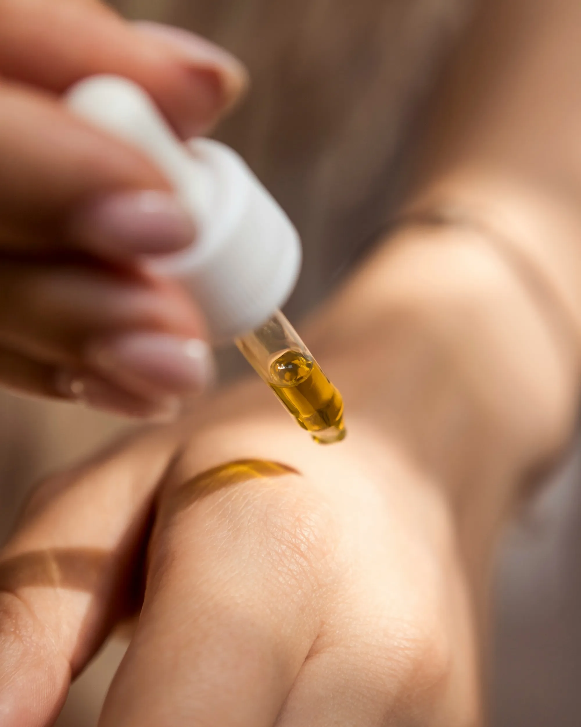 Eine Hand trägt mit einer Pipette einen Tropfen CBD-Öl auf den Handrücken auf